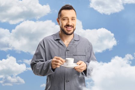 Photo for Man in pajamas holding a cup of espresso coffee with clouds and sky as a background - Royalty Free Image