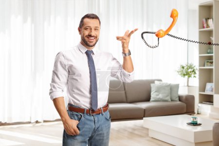 Photo for Cheerful man throwing a rotary phone handset in a living room - Royalty Free Image