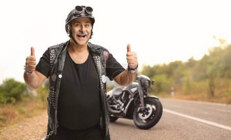 Téléchargez les photos : Homme mature motard avec un gilet en cuir montrant pouces sur la route - en image libre de droit