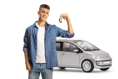 Foto de Hombre adolescente sosteniendo una llave de coche y de pie delante de un coche plateado aislado sobre fondo blanco - Imagen libre de derechos
