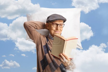 Téléchargez les photos : Homme âgé reposant sur un oreiller et lisant un livre parmi les nuages dans le ciel - en image libre de droit