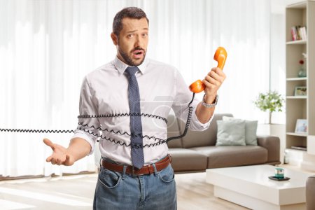 Photo for Surprised young man tied with a rotary phone cable at home in a living room - Royalty Free Image