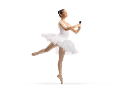 Foto de Foto completa de una bailarina bailando y sosteniendo un smartphone aislado sobre fondo blanco - Imagen libre de derechos