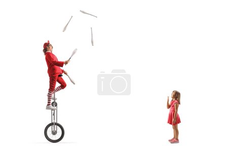 Téléchargez les photos : Fille excitée regarder un acrobate chevaucher une girafe monocycle et jongler isolé sur fond blanc - en image libre de droit