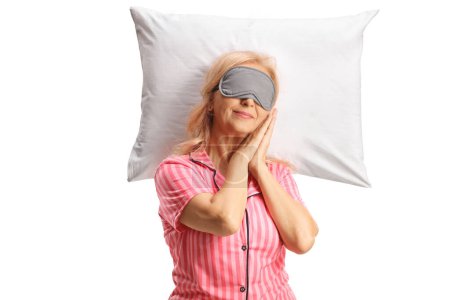 Téléchargez les photos : Femme mûre avec un masque dormant paisiblement sur un oreiller isolé sur fond blanc - en image libre de droit
