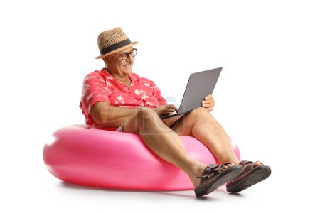Photo for Cheerful mature man sitting on a swimming ring and using a laptop computer isolated on white background - Royalty Free Image