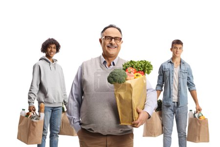 Téléchargez les photos : Homme mûr souriant debout devant de jeunes hommes avec des sacs d'épicerie isolés sur fond blanc - en image libre de droit
