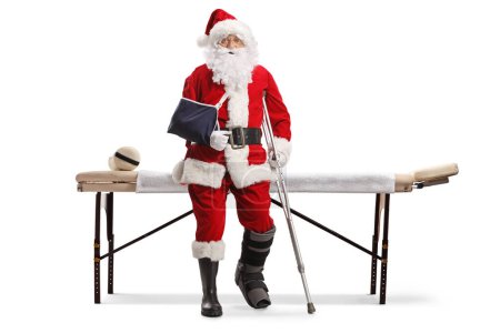 Téléchargez les photos : Père Noël avec jambe et bras blessés debout devant une table de natte isolée sur fond blanc - en image libre de droit
