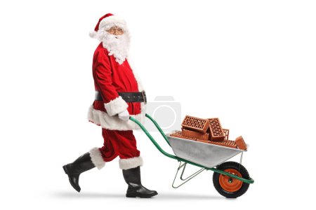 Photo for Full length shot of santa claus pushing a wheelbarrow with bricks isolated on white background - Royalty Free Image