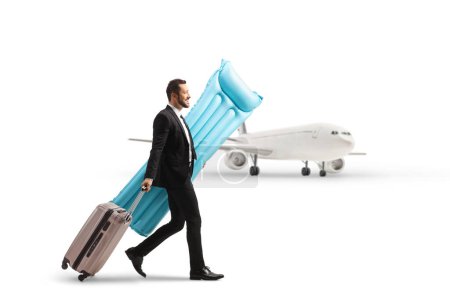 Photo for Businessman carrying a swim floating mattress and pullung a suitcase at the airport isolated on white background - Royalty Free Image