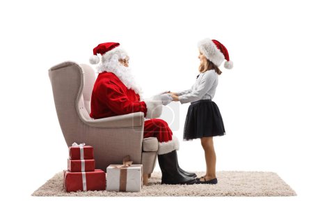 Photo for Santa claus sitting in an armchair and holding hands with a little girl isolated on white background - Royalty Free Image