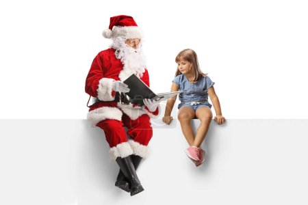 Téléchargez les photos : Père Noël assis sur un panneau vierge et lisant un livre à une petite fille isolée sur fond blanc - en image libre de droit