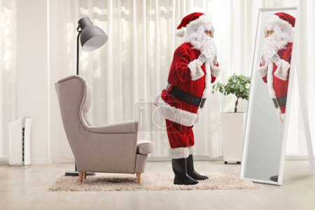 Téléchargez les photos : Plan de profil complet du Père Noël se préparant devant un miroir à la maison - en image libre de droit