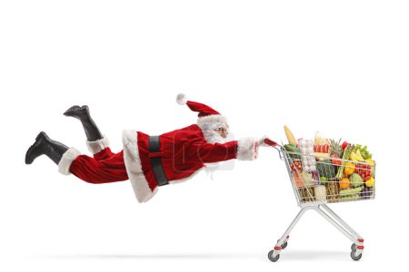 Photo for Santa claus flaying and holding a shopping cart with food isolated on white background - Royalty Free Image