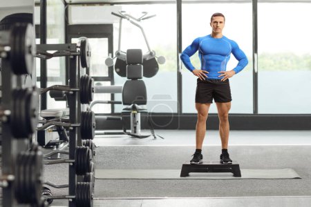 Photo for Full length portrait of a muscular man standing on a step aerobic platform at a gym - Royalty Free Image