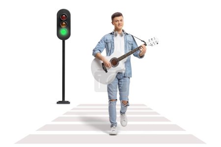 Téléchargez les photos : Jeune homme jouant de la guitare acoustique et traversant une rue à un passage piétonnier isolé sur fond blanc - en image libre de droit