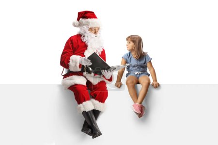 Foto de Santa Claus sentado en un panel en blanco y leyendo una historia a una niña aislada sobre fondo blanco - Imagen libre de derechos