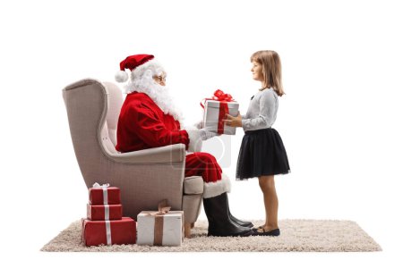 Téléchargez les photos : Père Noël assis dans un fauteuil et donnant un cadeau à un enfant isolé sur fond blanc - en image libre de droit