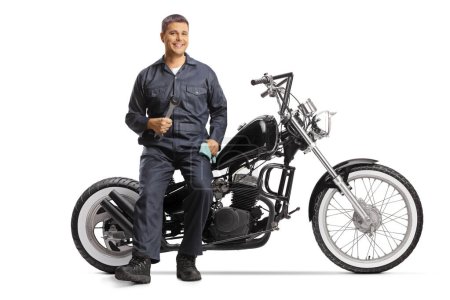 Téléchargez les photos : Mécanicien assis sur une moto et souriant isolé sur fond blanc - en image libre de droit