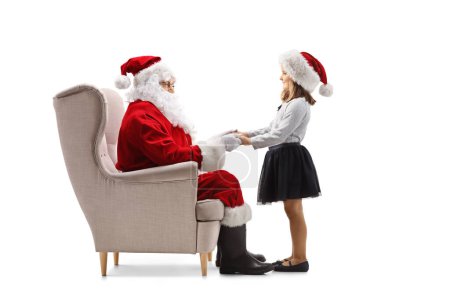 Foto de Santa Claus sentada en un sillón hablando con una chica y sosteniendo sus manos aisladas sobre fondo blanco - Imagen libre de derechos