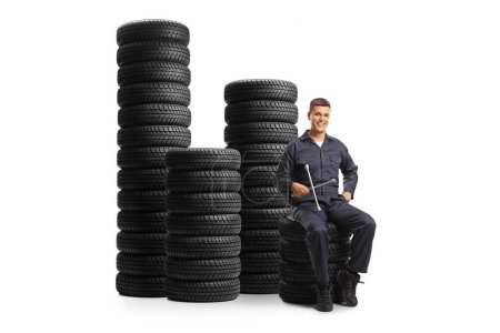 Photo for Auto mechanic sitting on a pile of tires and holding a wrench tool isolated on white background - Royalty Free Image