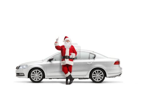 Photo for Santa claus leaning on a silver car and pointing up isolated on white background - Royalty Free Image
