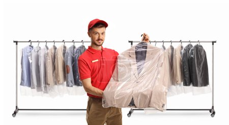 Foto de Trabajador de limpieza en seco sosteniendo un traje en una funda de bolsa de plástico delante de la ropa colgada en un estante aislado en un fondo blanco - Imagen libre de derechos