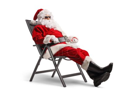 Téléchargez les photos : Père Noël avec des lunettes de soleil assis sur une chaise pliable isolé sur fond blanc - en image libre de droit