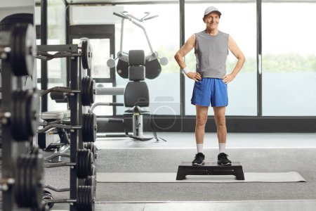 Photo for Full length portrait of an elderly man in sportswear standing on a step aerobic platform at a gym - Royalty Free Image