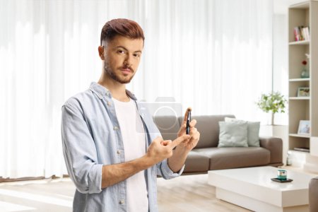 Téléchargez les photos : Jeune homme poing doigt avec un dispositif lancette à la maison dans un salon - en image libre de droit
