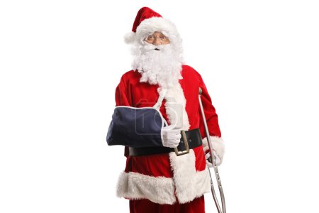 Téléchargez les photos : Père Noël avec bras blessé appuyé sur une béquille isolée sur fond blanc - en image libre de droit