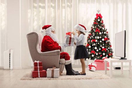 Photo for Excited little girl opening a gift box in front of santa at home in a living roo - Royalty Free Image