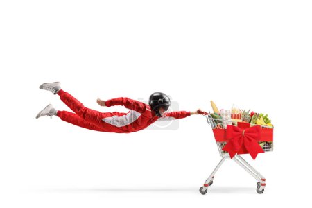 Foto de Corredor de coches volando y sosteniendo un carrito de compras con comida y lazo rojo aislado sobre fondo blanco - Imagen libre de derechos
