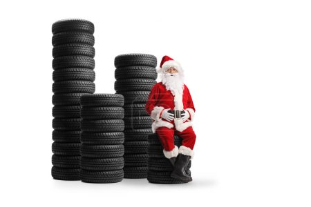 Téléchargez les photos : Père Noël assis sur un tas de pneus de voiture isolé sur fond blanc - en image libre de droit