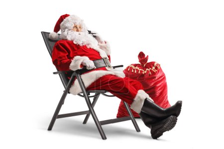 Photo for Santa claus sitting in a foldable chair and making a phone call isolated on white background - Royalty Free Image