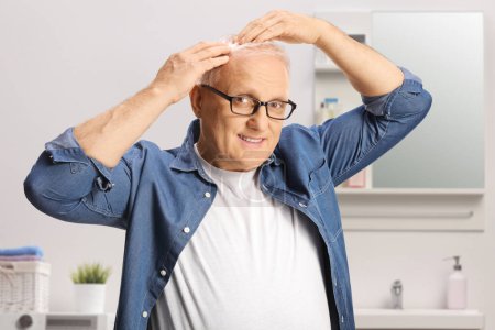 Téléchargez les photos : Mature homme dans une salle de bain vérifier ses cheveux - en image libre de droit