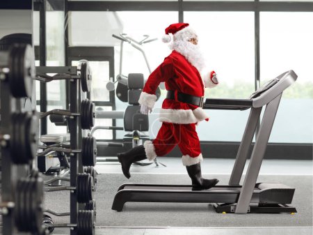 Téléchargez les photos : Profil complet du Père Noël en course sur un tapis roulant dans une salle de gym - en image libre de droit