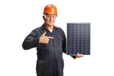 Foto de Trabajador con casco en uniforme sujetando un panel fotovoltaico y apuntando aislado sobre fondo blanco - Imagen libre de derechos
