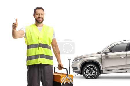 Téléchargez les photos : Travailleur de l'assistance routière tenant une boîte à outils et gesticulant les pouces devant un VUS avec pneu crevé isolé sur fond blanc - en image libre de droit
