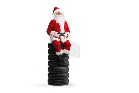 Téléchargez les photos : Père Noël assis sur un tas de pneus de véhicule isolé sur fond blanc - en image libre de droit