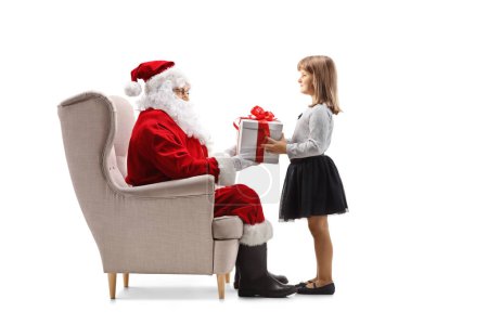 Téléchargez les photos : Père Noël assis dans un fauteuil donnant un cadeau à un enfant isolé sur fond blanc - en image libre de droit