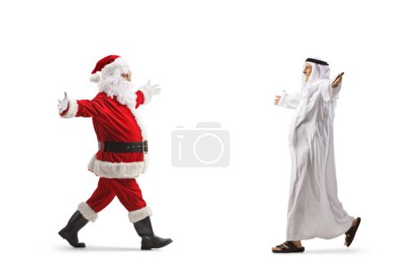 Foto de Santa Claus caminando hacia un hombre musulmán maduro con ropa étnica aislada sobre fondo blanco - Imagen libre de derechos