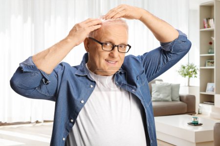 Téléchargez les photos : Mature homme vérifier ses cheveux blancs à la maison dans un salon - en image libre de droit