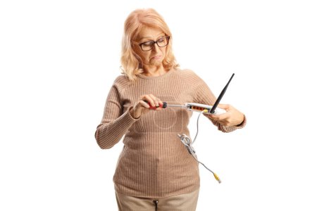 Téléchargez les photos : Femme mature confuse fixant un routeur avec un tournevis isolé sur fond blanc - en image libre de droit
