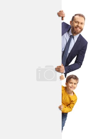 Téléchargez les photos : Mignon garçon et un homme regardant de derrière un panneau blanc vide isolé sur fond blanc - en image libre de droit
