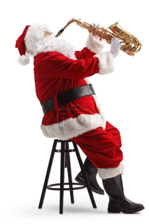 Téléchargez les photos : Photo de profil pleine longueur du Père Noël assis sur une chaise et jouant un saxophone isolé sur fond blanc - en image libre de droit