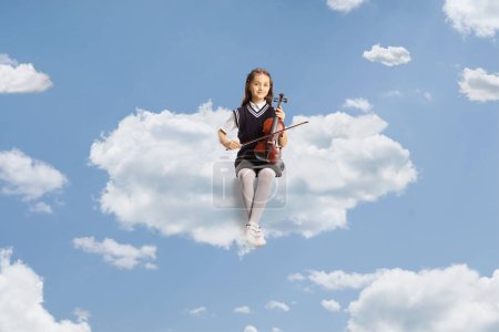 Photo for Schoolgirl sitting on a cloud and holding a violin up in the sky - Royalty Free Image