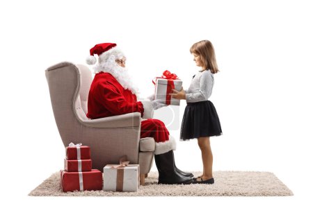 Téléchargez les photos : Père Noël assis dans un fauteuil et donnant une boîte béante à une fille isolée sur fond blanc - en image libre de droit