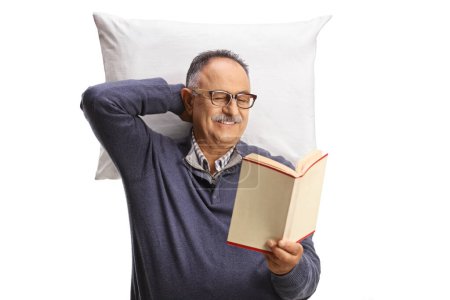 Foto de Hombre maduro descansando sobre una almohada y leyendo un libro aislado sobre fondo blanco - Imagen libre de derechos