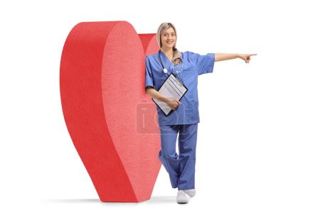 Photo for Full length portrait of a female cardiologist gesturing pointing and leaning on a red heart, cardiology and health care concept - Royalty Free Image